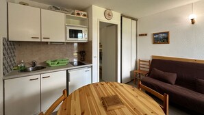 A compact kitchen with a microwave, sink, and cabinets. There's a dining table with chairs and a brown sofa in the living area. - Ski-in apartment for 5 people, balcony, Morillon 1100 (Morillon 1100)