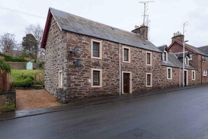 A stone building with a gabled roof, multiple windows, and a door. - Ground Floor Apartment W/large Enclosed Garden (Crieff)