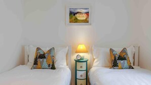 A hotel room with two beds, each with matching decorative pillows, a bedside table with a lamp, and a framed picture on the wall. - Ground Floor Apartment W/large Enclosed Garden (Crieff)