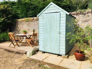 A small shed with a door, a table with chairs, and a potted plant. - Ground Floor Apartment W/large Enclosed Garden (Crieff)