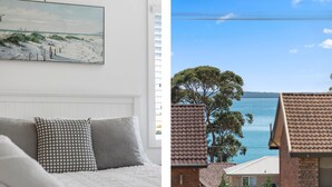Een slaapkamer met een wit hoofdeinde, gekleurde kussens en een schilderij van een strand.