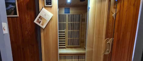 A wooden sauna with a control panel, ventilation system, and a small poster on the wall.