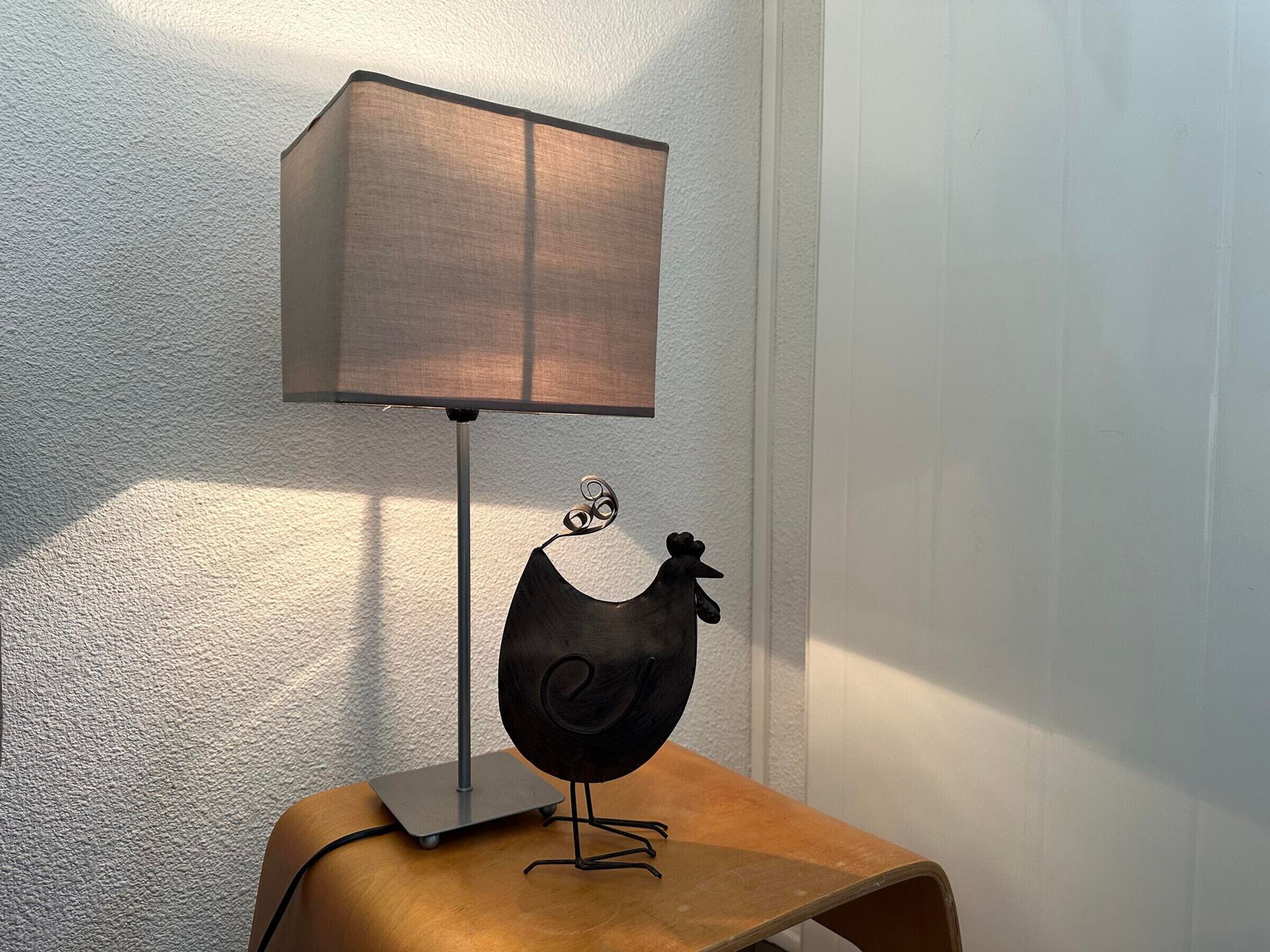 A lamp with a square shade and a black metal stand on a wooden stool.
