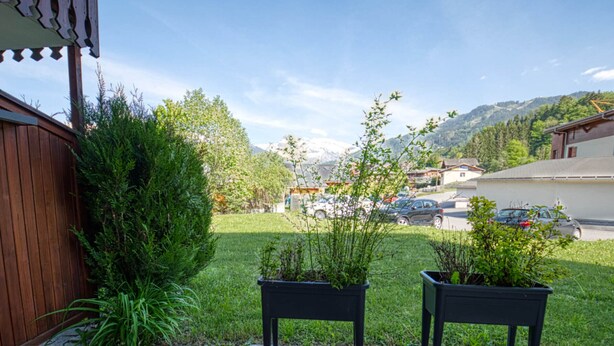 A patio area with two black planters, a wooden bench, and a view of a parking lot and buildings in the background. - Renovated apartment near lake and shuttle, 4 pers, non-smoking, no internet (Morillon Village)