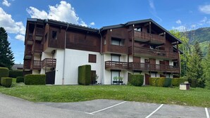 A multi-story building with balconies, a parking lot, and a mountainous backdrop. - Renovated apartment near lake and shuttle, 4 pers, non-smoking, no internet (Morillon Village)