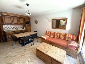A compact living space with a kitchenette, a dining table, a sofa, and a wooden bench.