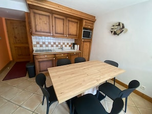 A compact kitchen with wooden cabinets, a tiled backsplash, a built-in microwave, and a dining area with a wooden table and black chairs. - Apartment for 7, ski-in/ski-out, balcony (Morillon 1100)