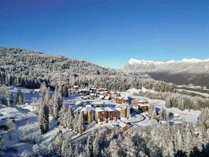 A snow-covered resort with multiple buildings, ski slopes, and a mountainous backdrop.