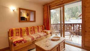 Ein Holzinnenraum mit einer Couch, einem Holztisch und einem Balkon mit Stühlen.