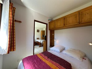 Une chambre à coucher avec un lit, une armoire en bois, un miroir et une fenêtre avec des rideaux.