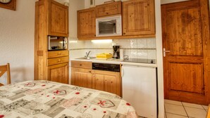 Eine kompakte Küche mit Holzschränken, einer Mikrowelle, einer Kaffeemaschine und einem Kühlschrank.