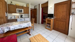 A compact kitchen with wooden cabinets, a dining table, and a bench. There is a television on a wooden stand and a red curtain in the background. - Cozy apartment for 6 with mountain balcony (Morillon 1100)
