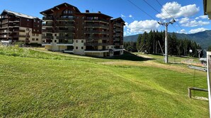 A multi-story building with balconies, situated on a grassy slope with mountains in the background. - Cozy apartment for 6 with mountain balcony (Morillon 1100)