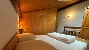 Un dormitorio con cabecera de madera, cama con ropa de cama blanca, mesita de noche con lámpara y una silla de madera.