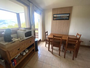 Un coin repas avec une table et des chaises en bois, un four à micro-ondes posé sur un meuble en bois, et une fenêtre avec des rideaux.