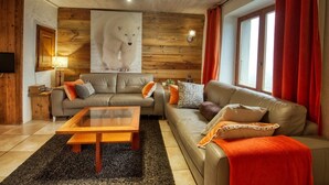 A cozy living room with a wooden ceiling, a large bear poster, two sofas, a coffee table, and a window with red curtains. - Charming apartment in renovated farmhouse, sauna & terrace (Morillon Village)