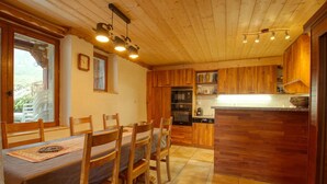 A wooden interior with a dining table and chairs, a kitchen with wooden cabinets, and a window with a view. - Charming apartment in renovated farmhouse, sauna & terrace (Morillon Village)