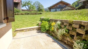 A rural house with a stone wall, a gravel driveway, and a grassy hill in the background. - Comfortable apartment for 4 in a picturesque village (Morillon Village)