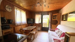 A cozy cabin interior with a wooden dining table, chairs, a sofa, a television, and a kitchen area with a coffee maker. - Comfortable apartment for 4 in a picturesque village (Morillon Village)