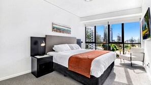 Une chambre d’hôtel moderne avec un grand lit, une table de chevet, un bureau et une chaise. Une grande fenêtre offre une vue sur la ville.