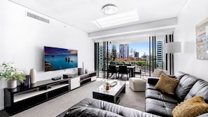Relax in this stylish living room with a large flat-screen TV, comfortable sofa, and sliding glass door leading to a balcony with city views.