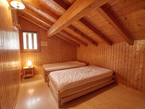 A wooden cabin bedroom with two single beds, a small window, and a nightstand with a lamp.