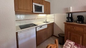 A compact kitchen with wooden cabinets, a microwave, a dishwasher, a refrigerator, and a coffee maker. - Charming 6-person apartment, balcony with mountain view, modern comfort, non-smoking (Morillon 1100)