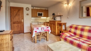 A compact living space with a dining table, wooden cabinets, a sofa, and a kitchenette. - Charming 6-person apartment, balcony with mountain view, modern comfort, non-smoking (Morillon 1100)