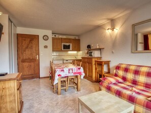 A compact living space with a dining table, wooden cabinets, a sofa, and a kitchenette. - Charming 6-person apartment, balcony with mountain view, modern comfort, non-smoking (Morillon 1100)