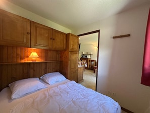 A bedroom with wooden cabinets, a bed with white bedding, and a nightstand with a lamp. - Charming 6-person apartment, balcony with mountain view, modern comfort, non-smoking (Morillon 1100)