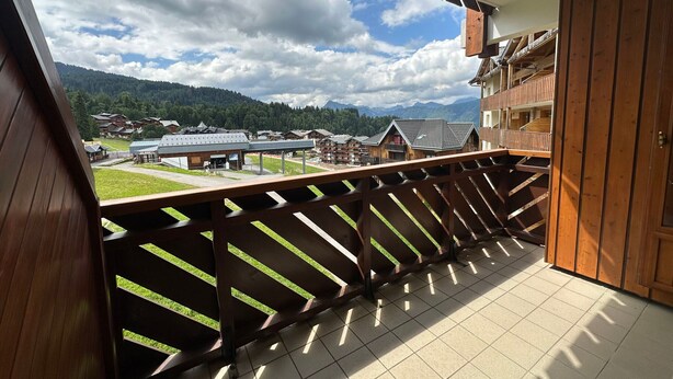 A balcony with a view of a mountainous landscape, wooden railings, and a tiled floor.