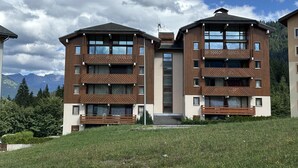A modern multi-story building with balconies, large windows, and a view of mountains in the background.