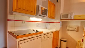 A compact kitchen with wooden cabinets, a microwave, a dishwasher, and a trash bin.