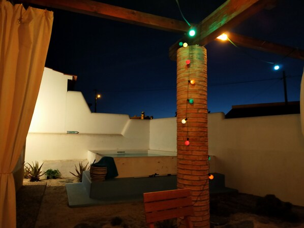 A rooftop patio with a brick column, string lights, and a bench.