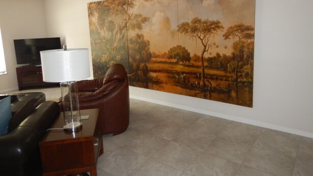 Uma sala de estar com um quadro de paisagem grande, um sofá de couro, uma televisão e um abajur.