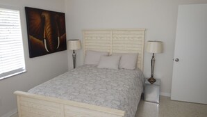 Quarto com cama de madeira, duas luminárias de cabeceira, uma porta e uma janela com persianas.