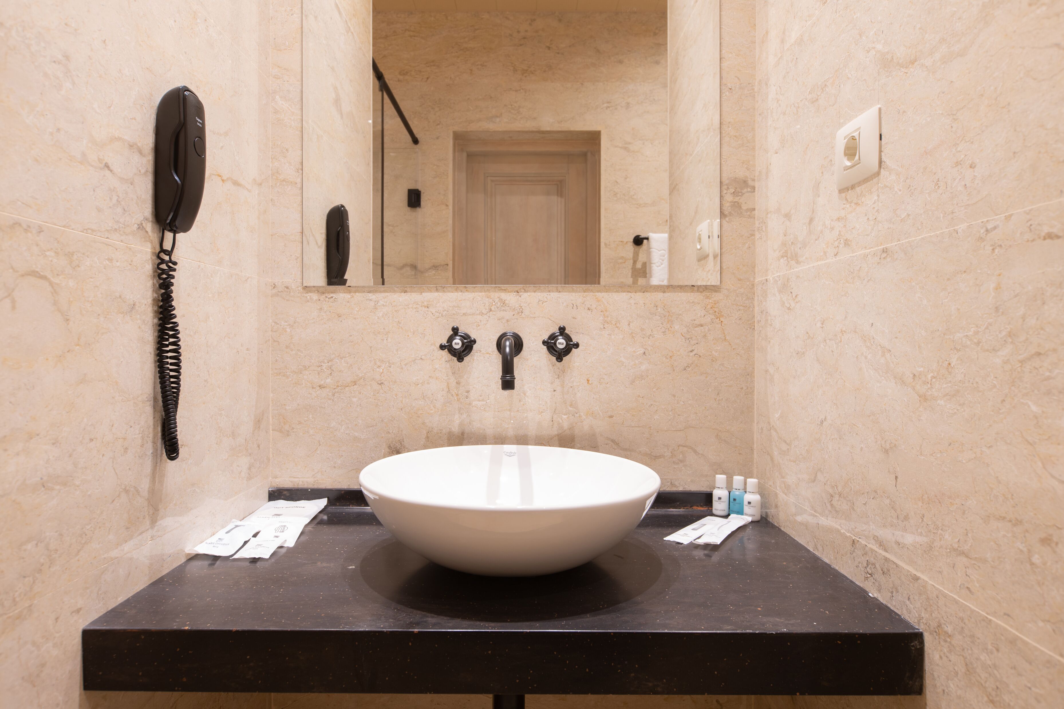 Ein Badezimmer mit einem weißen Waschbecken, einem Spiegel, einem Telefon und Toilettenartikeln auf der Ablagefläche.