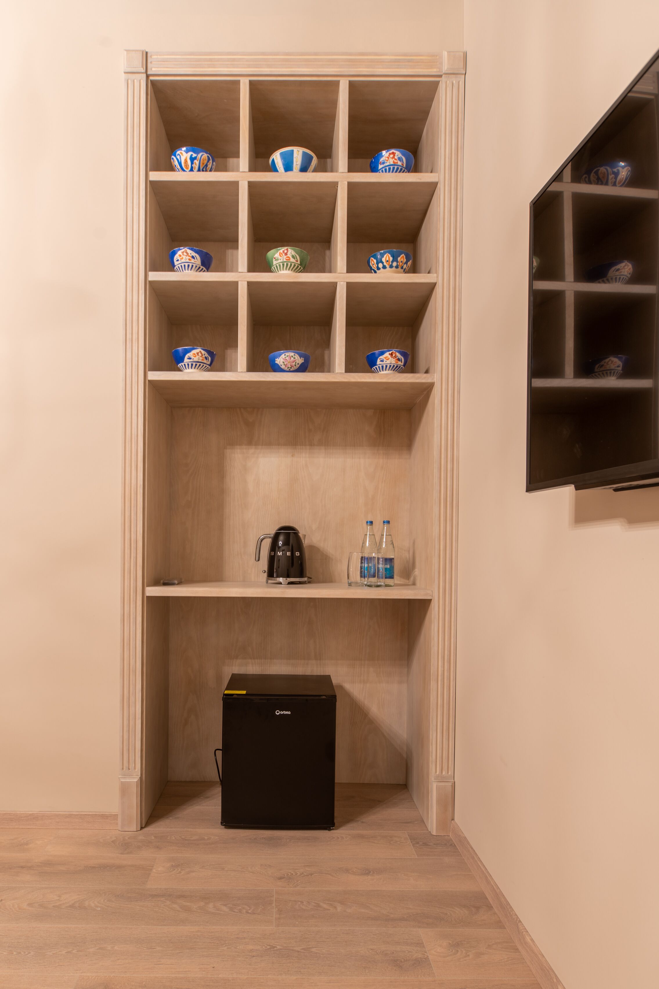 Un mueble de madera con varios estantes, algunos con cuencos y un hervidor, y una caja de almacenamiento negra en la parte inferior.