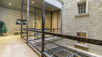 Un edificio de piedra con balcón, baranda de vidrio y planta en maceta.