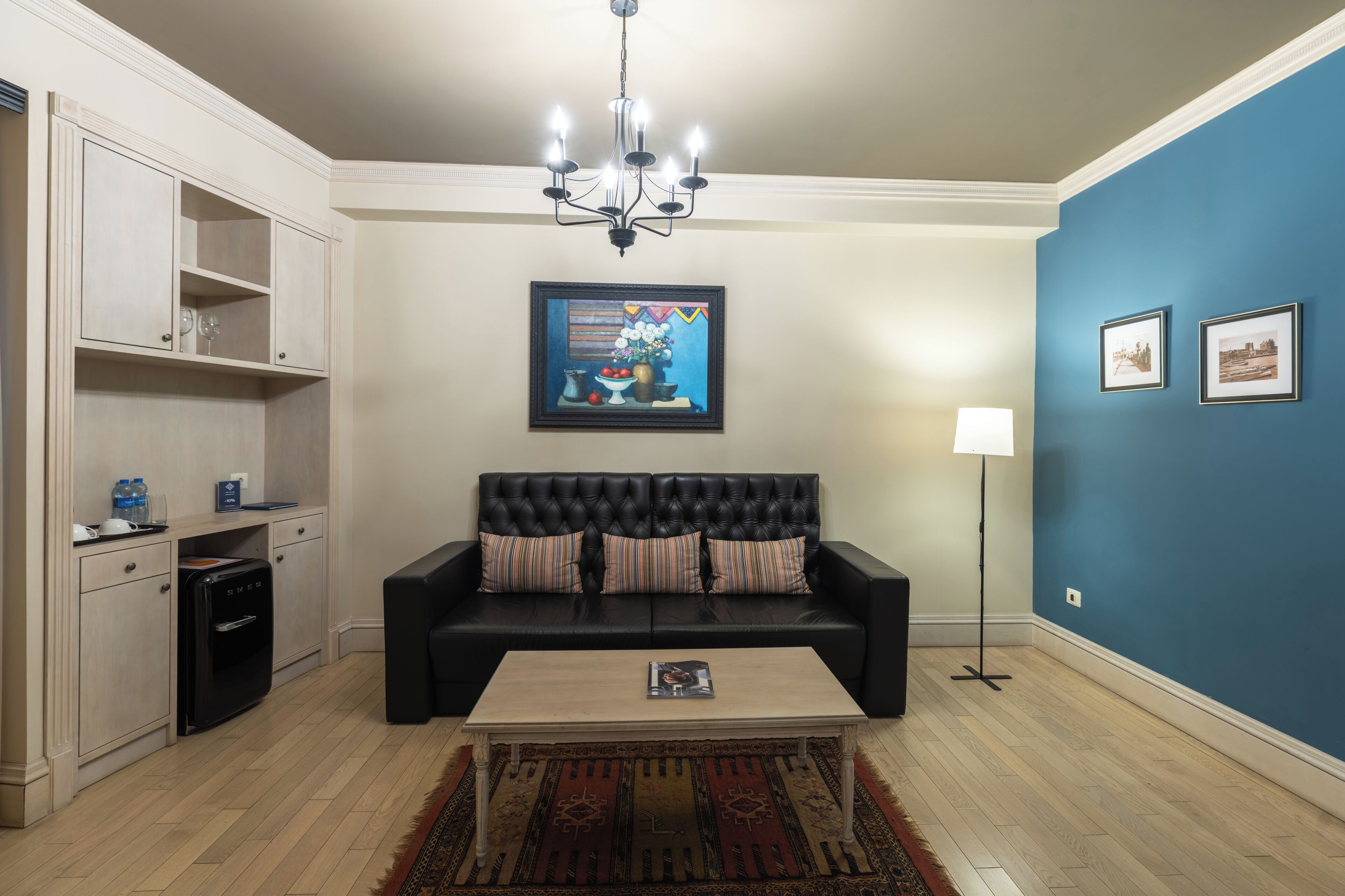 A living room with a black sofa, a coffee table, a chandelier, a painting, and a lamp.