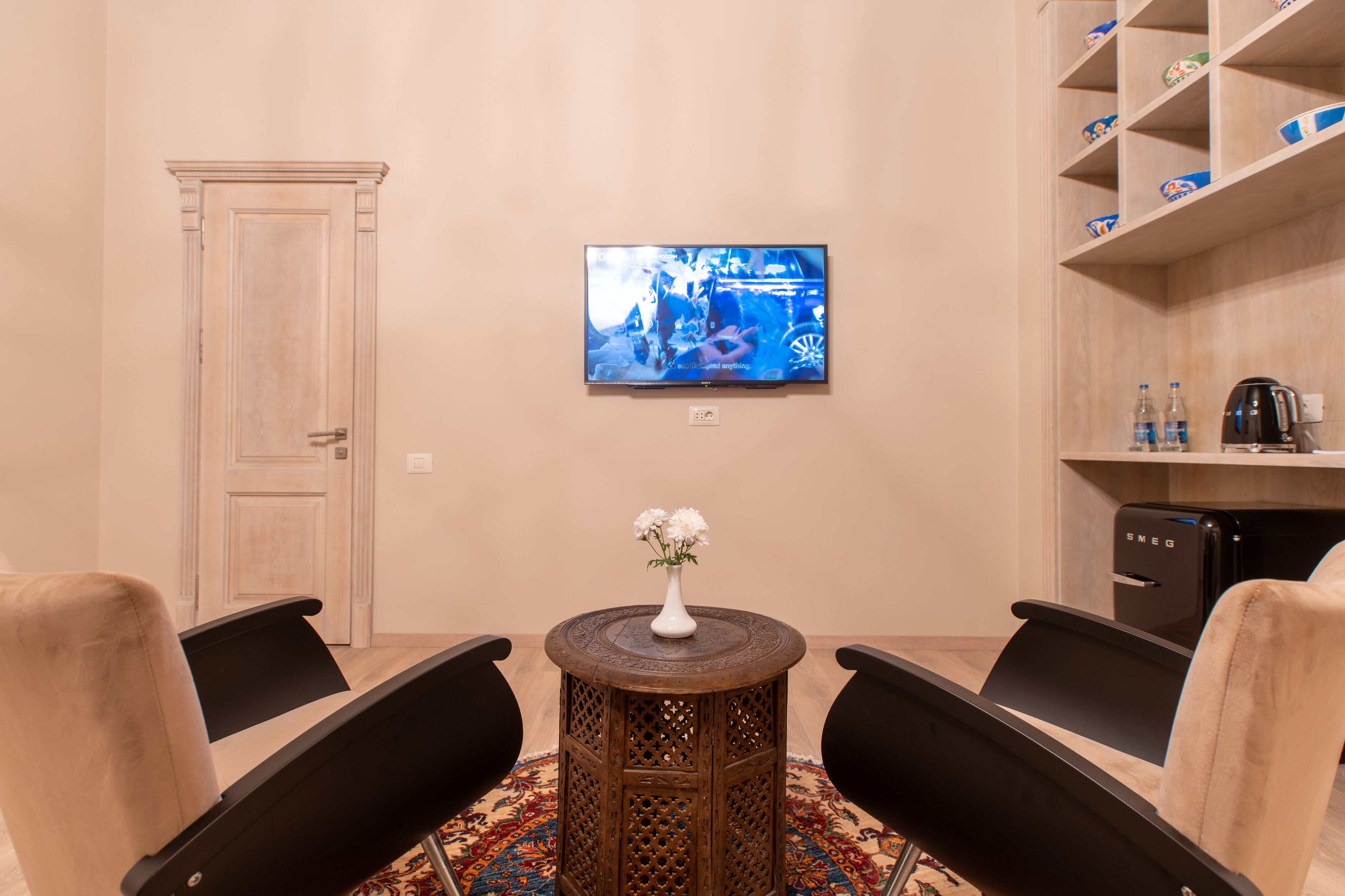 Una stanza con televisione a parete, un tavolino con un vaso, due sedie e una macchina da caffè.