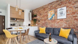 A modern living space with a kitchen, dining area, and a grey sofa with yellow cushions. - Stylish Apartment | Jacuzzi, Parking, Air Conditioning (Kraków)