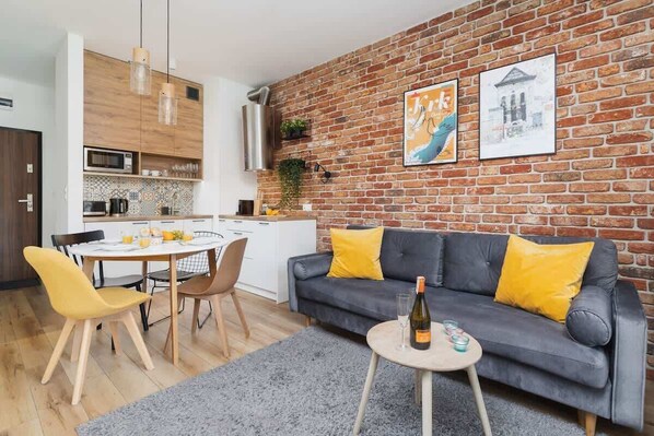 Un espace de vie moderne comprenant une cuisine, un coin repas et un canapé gris agrémenté de coussins jaunes.
