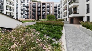 A modern apartment complex with multiple balconies, a landscaped garden area with flowers, and a paved walkway. - Stylish Apartment | Jacuzzi, Parking, Air Conditioning (Kraków)