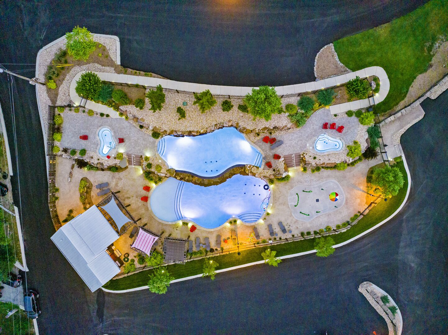 An aerial view of a resort with multiple swimming pools, a covered area, and a road adjacent to the property.