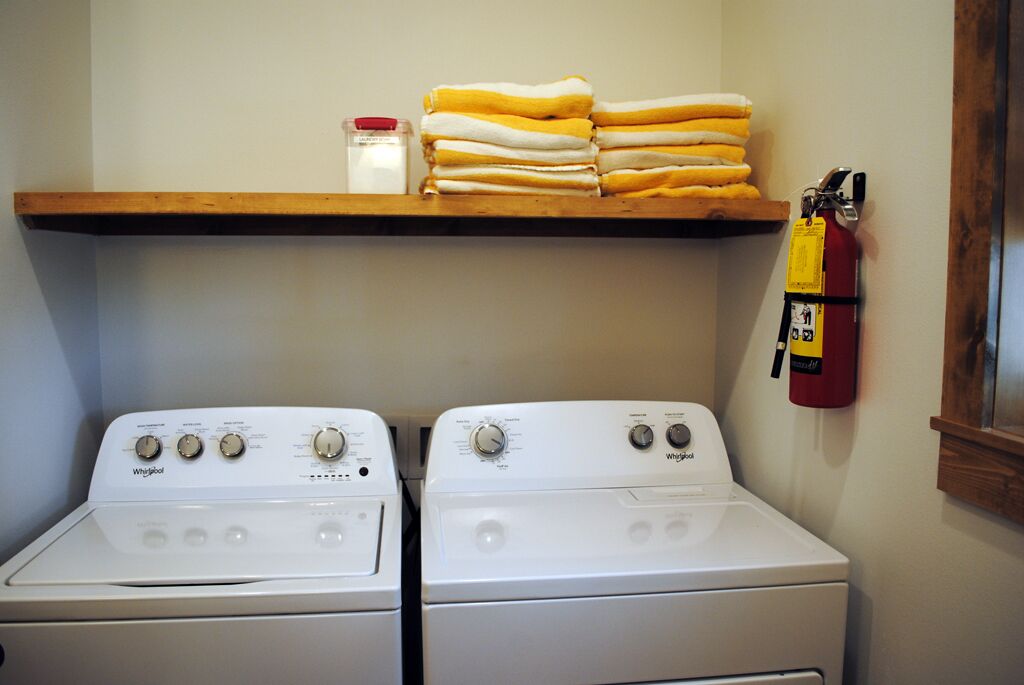 A laundry room with two Whirlpool washers and a shelf with folded towels.