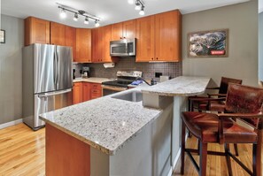 A modern kitchen with wooden cabinets, stainless steel appliances, granite countertops, and a bar area with leather chairs. - Nice Updated Condo. Hot Tub. Access to Lake. (Frisco)