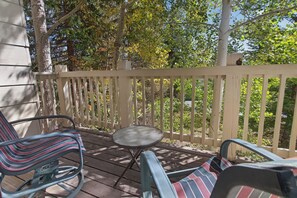 A wooden deck with two chairs and a small table, surrounded by a white fence and trees. - Nice Updated Condo. Hot Tub. Access to Lake. (Frisco)