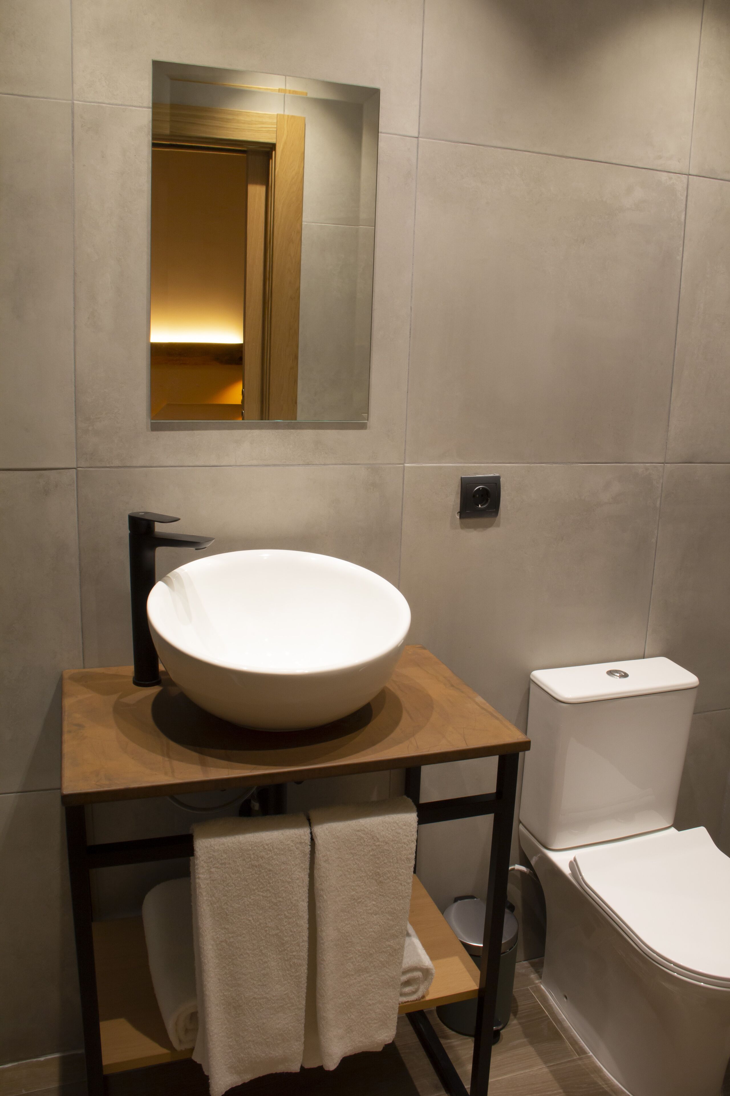 Un baño moderno con un lavamanos blanco de diseño, un mueble de tocador de madera, un espejo y un inodoro blanco.