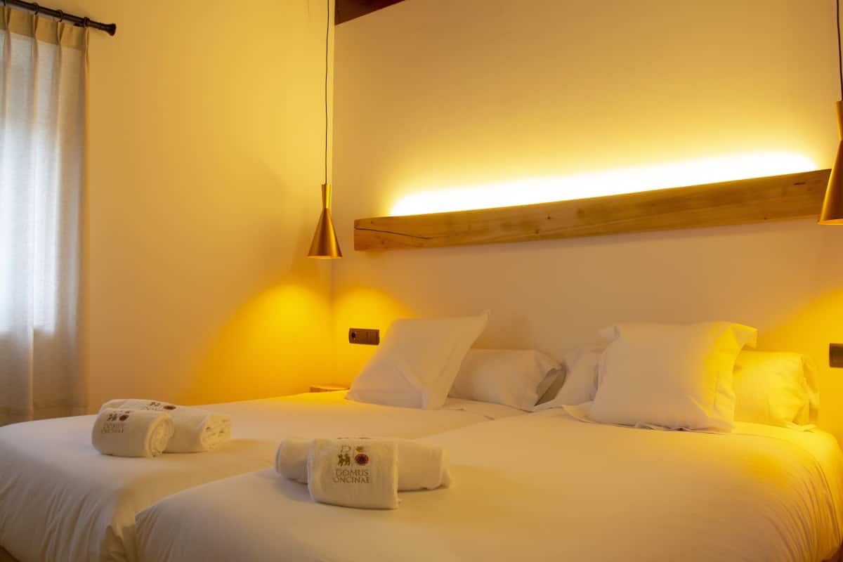 Une chambre d’hôtel avec un grand lit, deux tables de chevet, une tête de lit en bois et un luminaire suspendu.